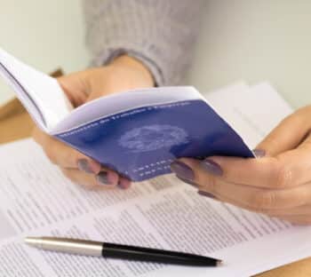 Female hands holding a A portfolio of Brazilian workers (Translation “Work Permit, Ministry of Labor and Social Security Brazil CTPS”). Contract and pen in background.